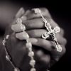 Young woman clasping rosary, close-up (B&W)