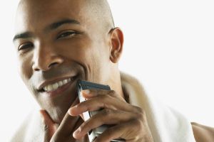 African American man shaving face with electric razor