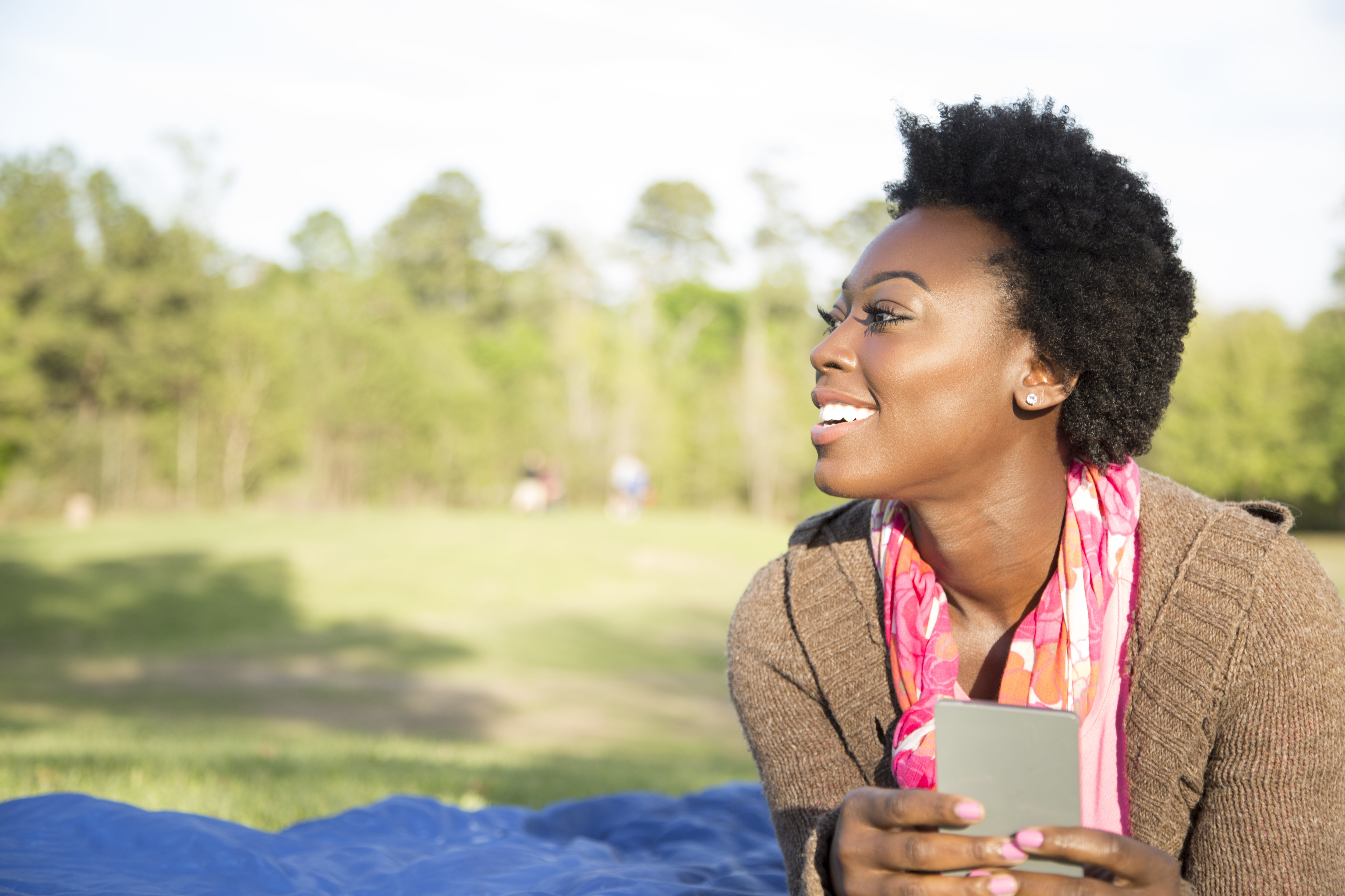 One African descent woman using cell phone outdoors in park.
