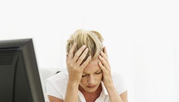 a woman sitting at a desk holding her head in pain