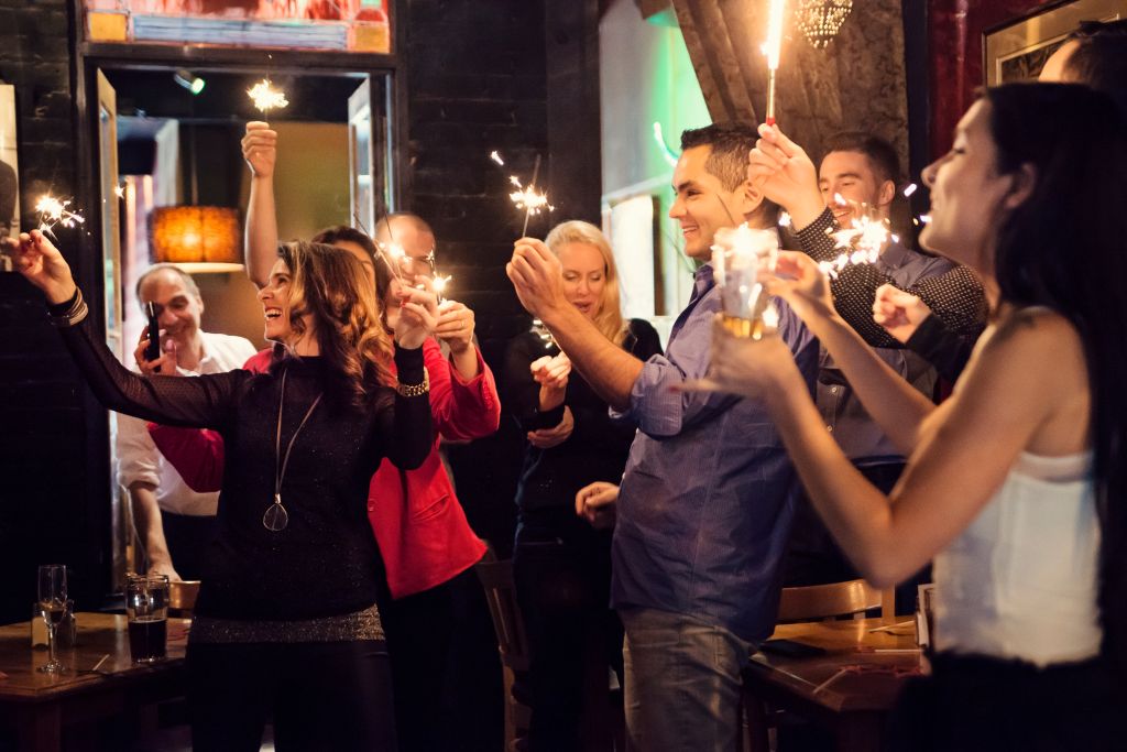 Friends and coworkers celebrating with sparklers in a bar.