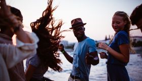 Young multi-ethnic hipster friends dancing at beach party at sunset