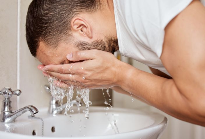 Shot of a young man washing his face in his bathroom sink