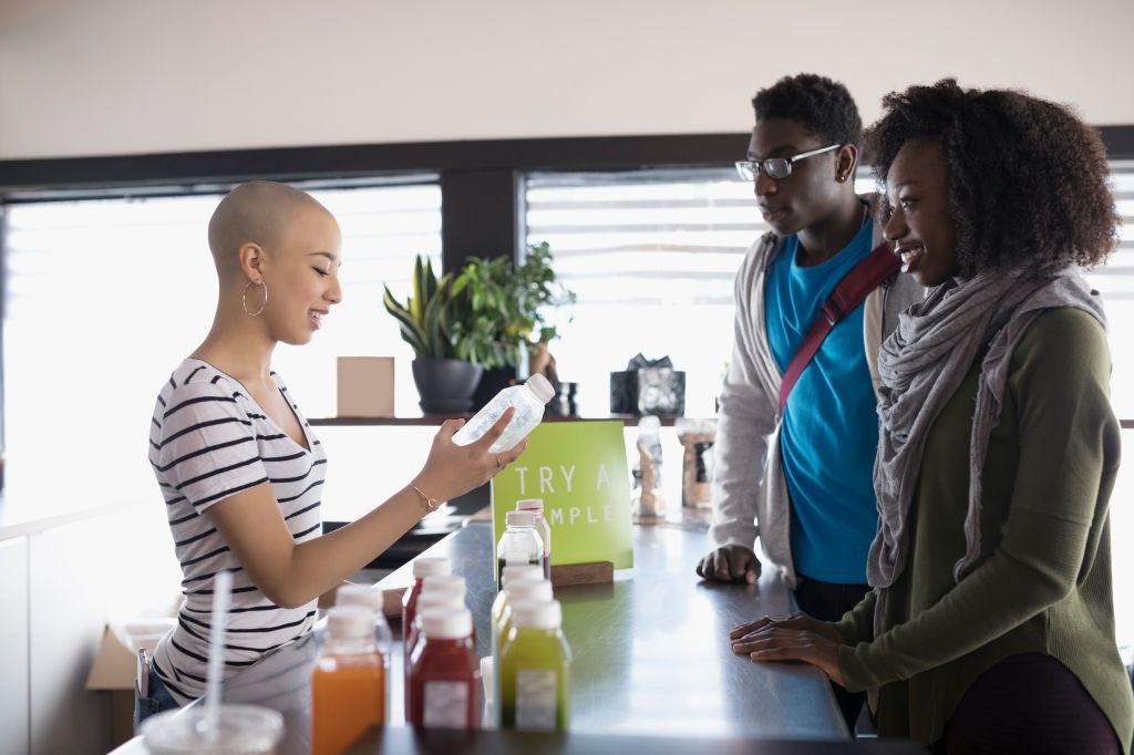 Teenage girl with shaved head working, helping customers at juice bar counter