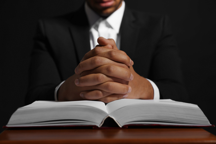 African American man with Bible praying to God at table on black background, closeup