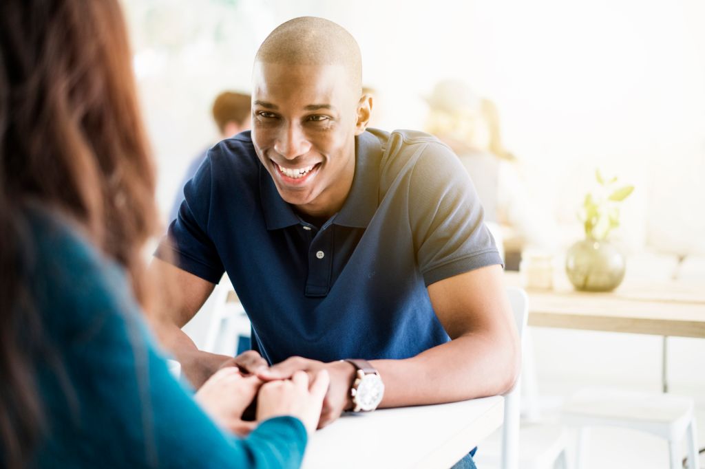 Smiling young man holding hands of woman in cafe