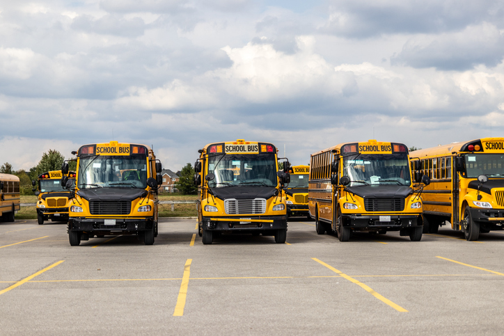 Yellow school buses lined up in an empty parking lot - under a partly cloudy sky