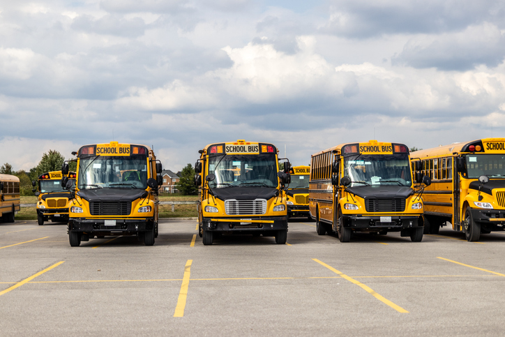 Yellow school buses lined up in an empty parking lot - under a partly cloudy sky