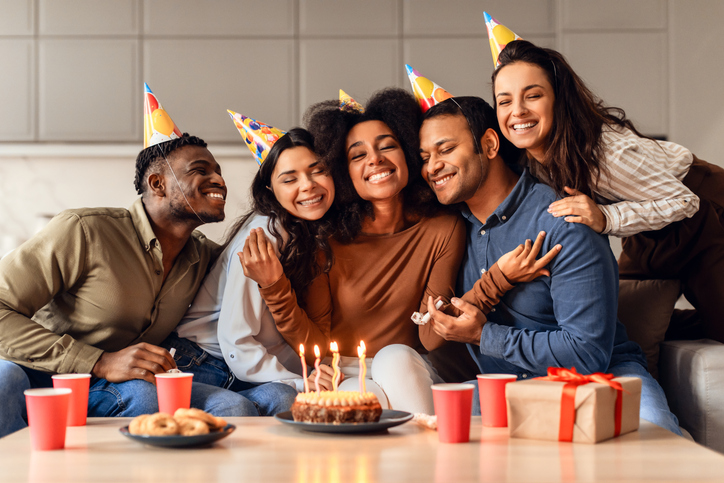Joyful multicultural friends hugging bday lady celebrating and partying indoor