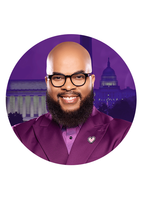 A smiling man with a beard wearing glasses and a purple shirt, with the U.S. Capitol building in the background.