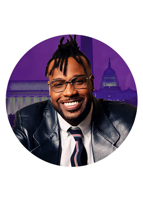 A smiling man wearing glasses and a suit, standing in front of the U.S. Capitol building at night.