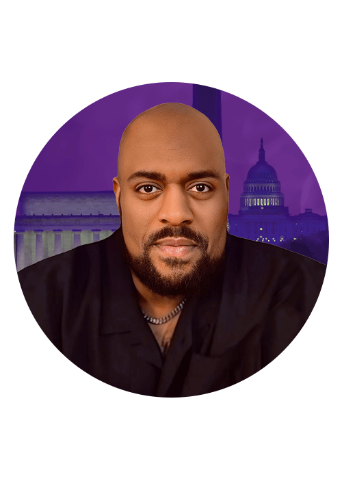 A headshot of a bald, bearded Black man wearing a black jacket, with the U.S. Capitol building illuminated in the background.